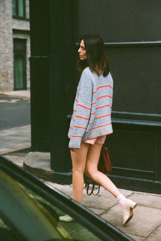 Woman wearing an oversized gray and red striped sweater walking on a street with red striped shorts