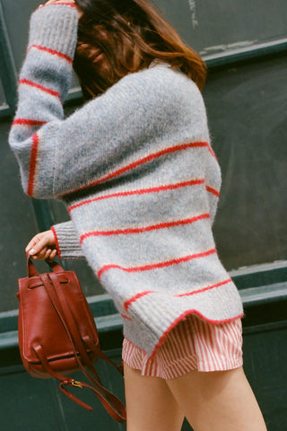 Woman wearing an oversized gray and red striped sweater with red striped shorts and holding a leather bag