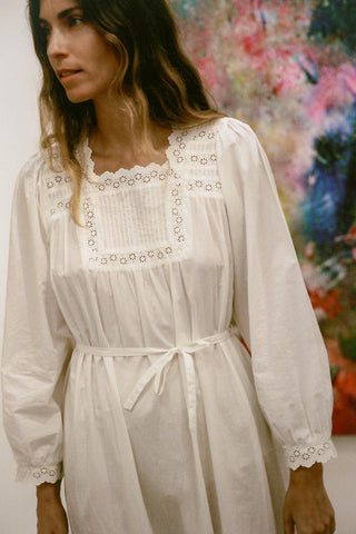 Woman wearing a white dress with lace details in an indoor setting.