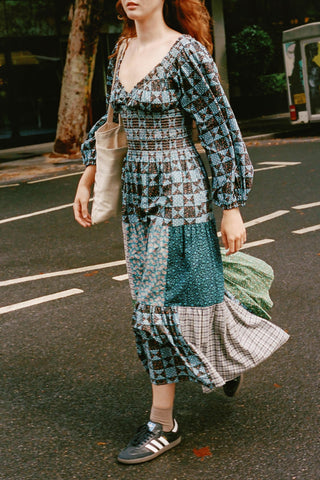 Woman wearing a patchwork dress with a tote on her shoulder walking on a street.