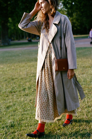 Woman in a trench coat and dress standing in a park