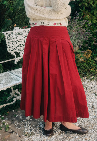 Close shot of a person wearing baggy red pants and a beige cardigan with a bench in the background 