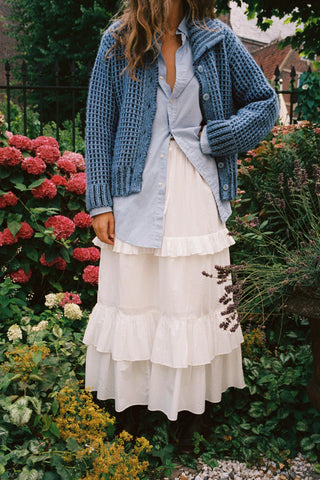 Woman wearing a gathered with skirt with tiers and ruffles with a chunky knit standing in a garden