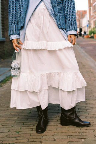 Person wearing a gathered with skirt with tiers and ruffles with a chunky knit standing on cobblestone