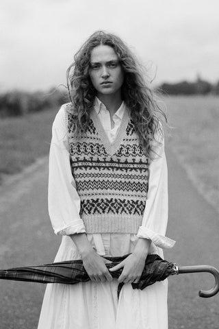 Black and white image of a woman wearing a vest over a shirt holding an umbrella