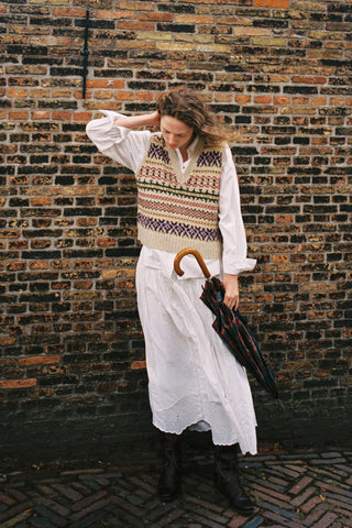 Woman wearing a colorful vest over a white shirt and skirt holding an umbrella