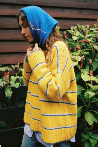 A woman wearing a bright yellow knit sweater with blue and white horizontal stripes, paired with a matching blue knit hood