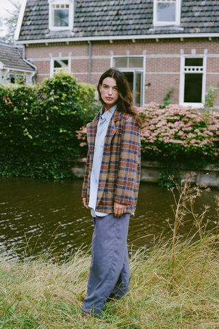 Women wearing a plaid blazer over the top of a blue shirt and pants standing by the water