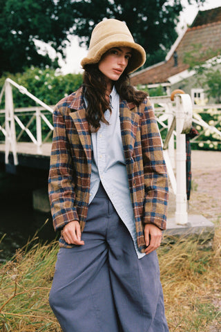 Women wearing a plaid blazer over the top of a blue shirt and pants with a cozy hat on