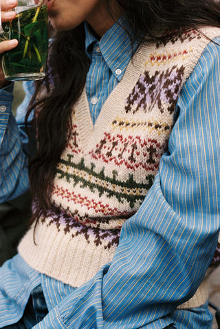 Person wearing a colorful vest over a blue pinstripe shirt