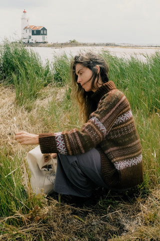 Woman wearing a patterned oversized sweater sitting in a field 
