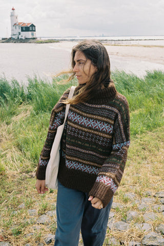 Woman wearing a patterned oversized sweater walking in a field with a bag on her shoulder