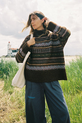 Woman wearing a patterned oversized sweater in a field with a bag on her shoulder