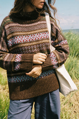 Woman wearing a patterned oversized sweater in a field with a bag on her shoulder