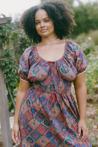 Woman wearing a patterned dress with a scoop neckline standing outdoors with greenery in the background
