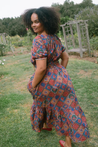 Woman wearing a patterned dress walking away from camera in a garden