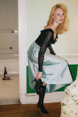 Woman in a light blue dress with black polka dot top and black high heels in a room.
