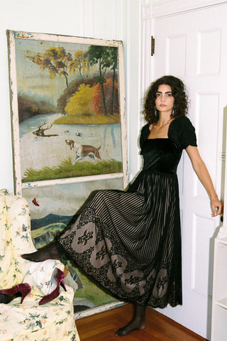 Woman in a black dress standing in a room with a large painting on the wall.