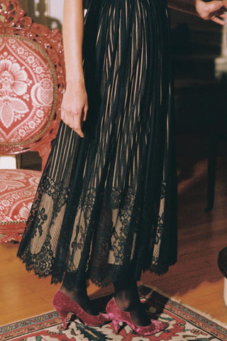 Person wearing a black lace dress with pink shoes in an indoor setting