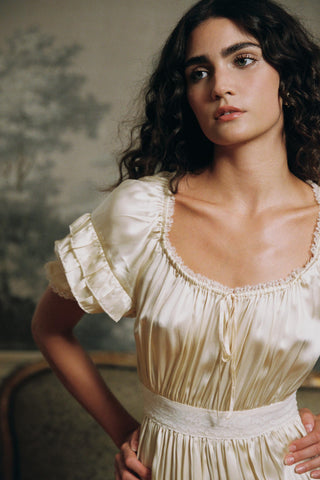 Woman wearing a vintage-style cream dress with ruffled sleeves in an indoor setting.