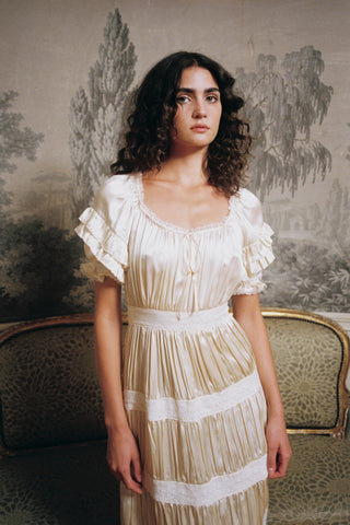 Woman wearing a white dress with ruffled sleeves in a vintage room.