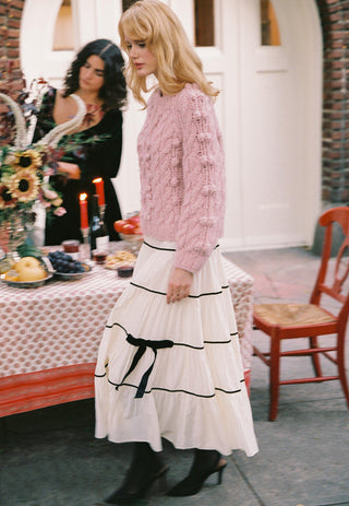 Woman walking in a rose colored cable knit sweater and white skirt