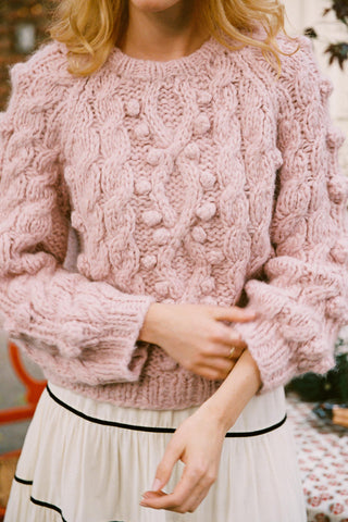 Woman wearing a rose colored cable knit sweater pulling up her sleeves