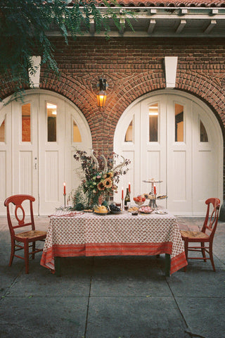 A floral block printed tablecloth with matching napkins on a large table with candles, fruit and flowers.