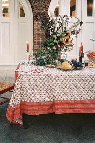 A floral block printed tablecloth on a decorated table with candles, fruit and flowers.