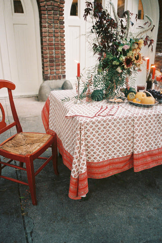 A floral block printed tablecloth with matching napkins on a large table with candles, fruit and flowers.