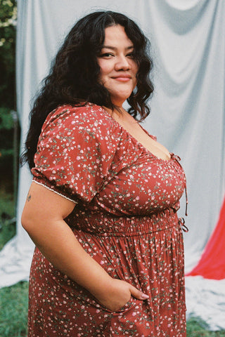 Woman wearing a red floral dress standing outdoors with a blue curtain in the background