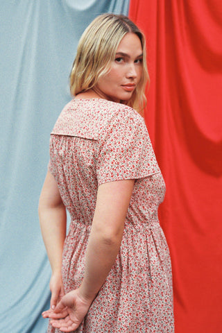Woman wearing a red floral dress against a red and blue curtain background
