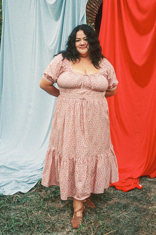 Woman wearing a red floral dress standing outdoors with a blue and red curtain in the background