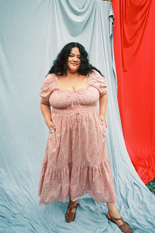 Woman wearing a red floral dress standing outdoors with a blue and red curtain in the background