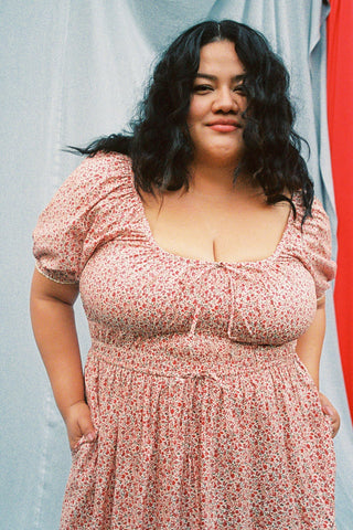 Woman wearing a red floral dress standing outdoors with a blue curtain in the background