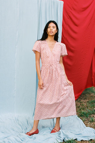 Woman wearing a red floral dress standing against a red and blue fabric background