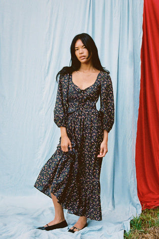 Woman wearing a floral dress standing against a light blue curtain with a red fabric.