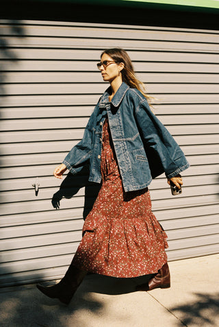 Woman wearing a denim jacket and floral dress against a gray wall.