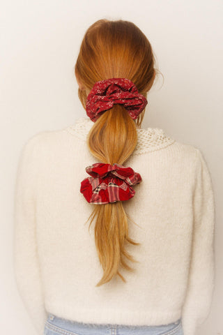 Person with red hair tied in a ponytail with two red scrunchies against a white background
