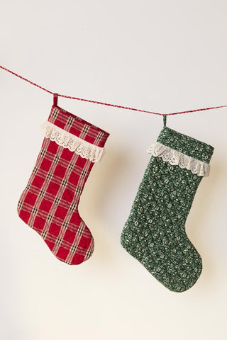 Two Christmas stockings, one red plaid and one green floral, hanging on a string against a white background.
