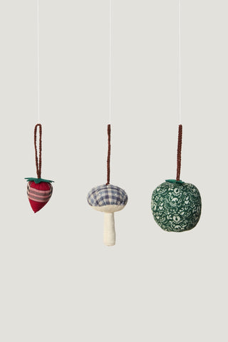 Decorative ornaments including a big green apple, a red and black striped strawberry, and a blue plaid mushroom hanging from white string.