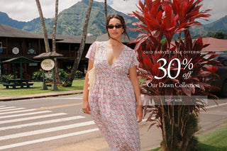 A woman wearing a short-sleeve V-neck floral dress stands outdoors on a street in front of mountains and palm trees, with a large promotional text overlay reading '30% off Our Dawn Collection' and 'Daily Harvest Sale Offering.'.