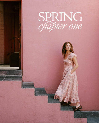 Woman in a dress standing on steps with 'Spring chapter one' text against a pink wall.