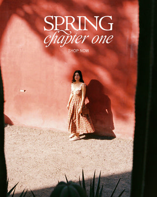 Woman in a red floral dress leaning against a bright red brick wall