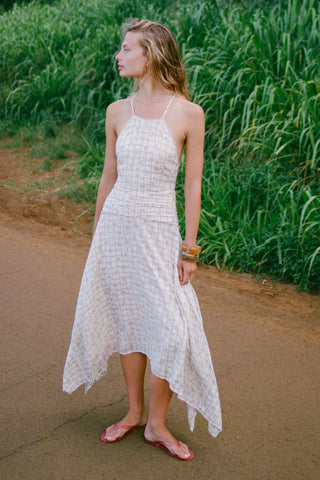 Woman in a white patterned dress standing on a dirt path with greenery around