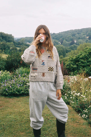 Woman in a patterned sweater and gray pants standing in a garden.