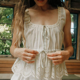 Woman wearing a light-colored sleeveless top with lace details outdoors.