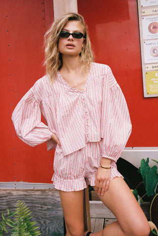 Woman in a red and white striped outfit standing in front of a red wall with a sign.