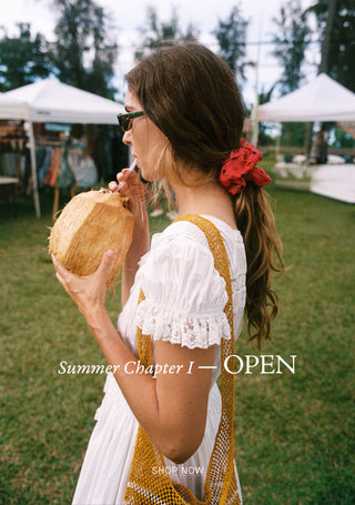 Woman in a white dress with yellow accents holding a coconut, with text overlay 'Summer Chapter I — OPEN' and 'SHOP NOW'.