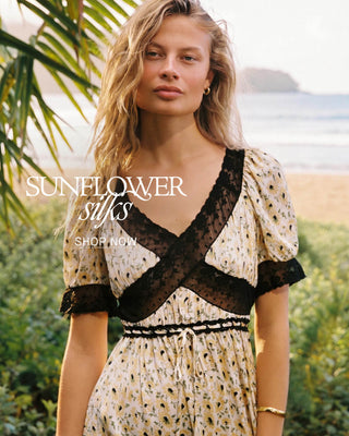 Woman wearing a floral dress with black lace details outdoors, with 'Sunflower Silks' branding.